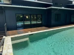 Wood pool deck with composite decking, black exterior wall, and sliding glass doors overlooking pool
