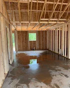 Interior room with wood framing studs, drywall installation on walls and ceiling, concrete floor
