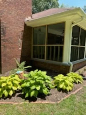 Yellow-green screened porch with railings attached to brick home