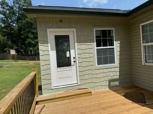 Newly built wooden deck with railing attached to home with vinyl siding and white entry door