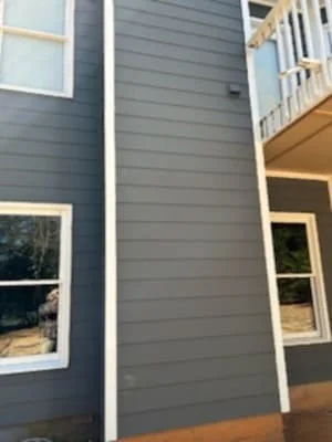 Gray fiber cement board siding with white trim around windows and deck framing