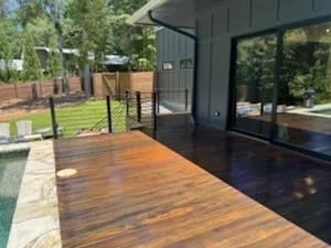 Stained wood deck with warm finish next to modern black-framed home and glass doors