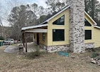 Stone chimney and wooden covered porch structure under construction with yellow framing