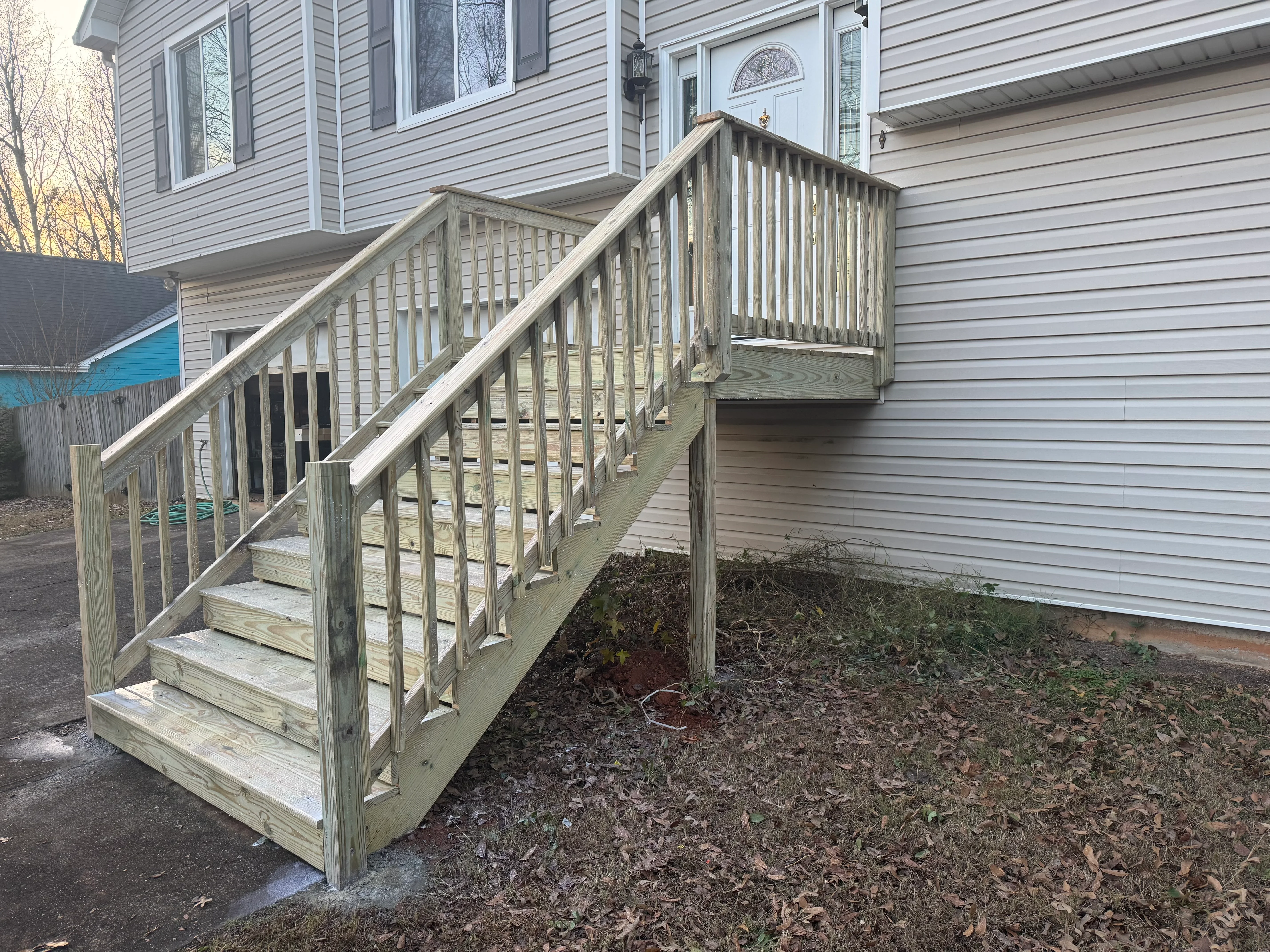 Elevated wooden deck with composite stairs, vertical spindle railings, and landing platform attached to house
