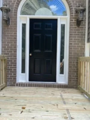 Pressure-treated wood deck with black entry door, white trim, and transom window on brick home